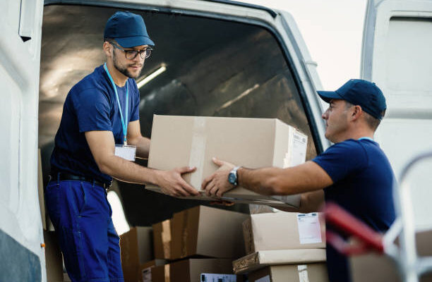 istockphoto-1186580104-612x612 Delivery men loading carboard boxes in a van while getting ready for the shipment.